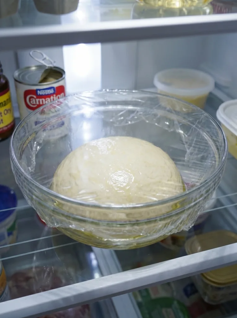 Beignet dough in oiled bowl covered for refrigerator chill