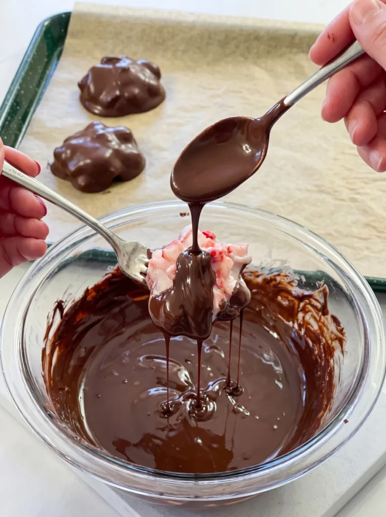 Dipping frozen strawberry yogurt cluster into melted chocolate coating