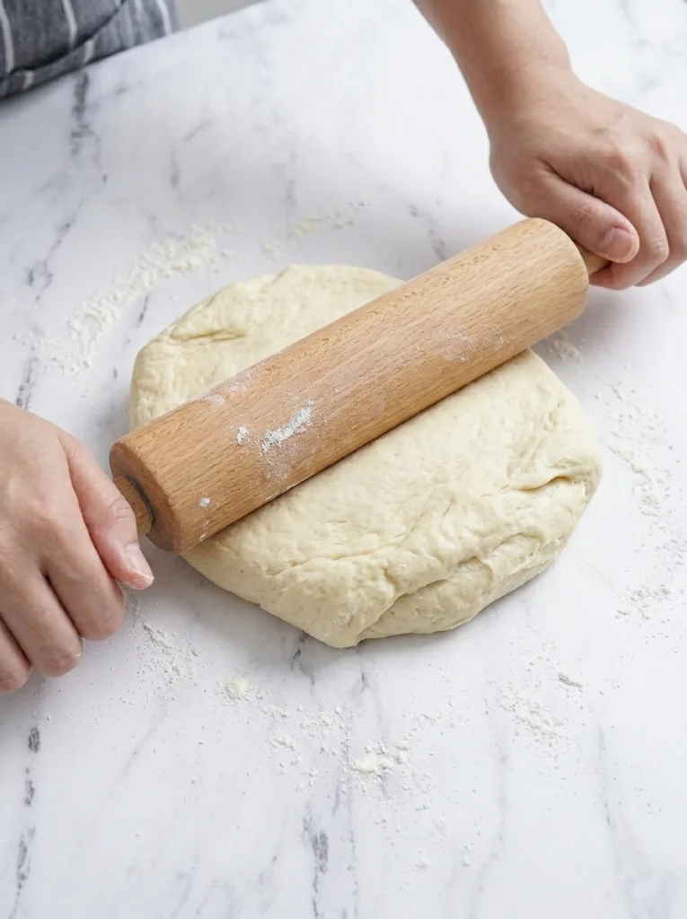 Rolling out chilled beignet dough on a floured surface to half inch thickness