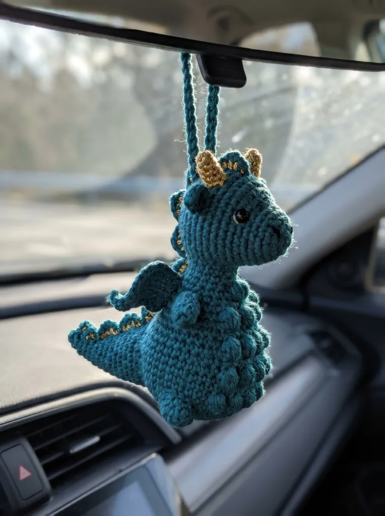 Small teal amigurumi dragon charm with gold horns and a bobble-stitch spine