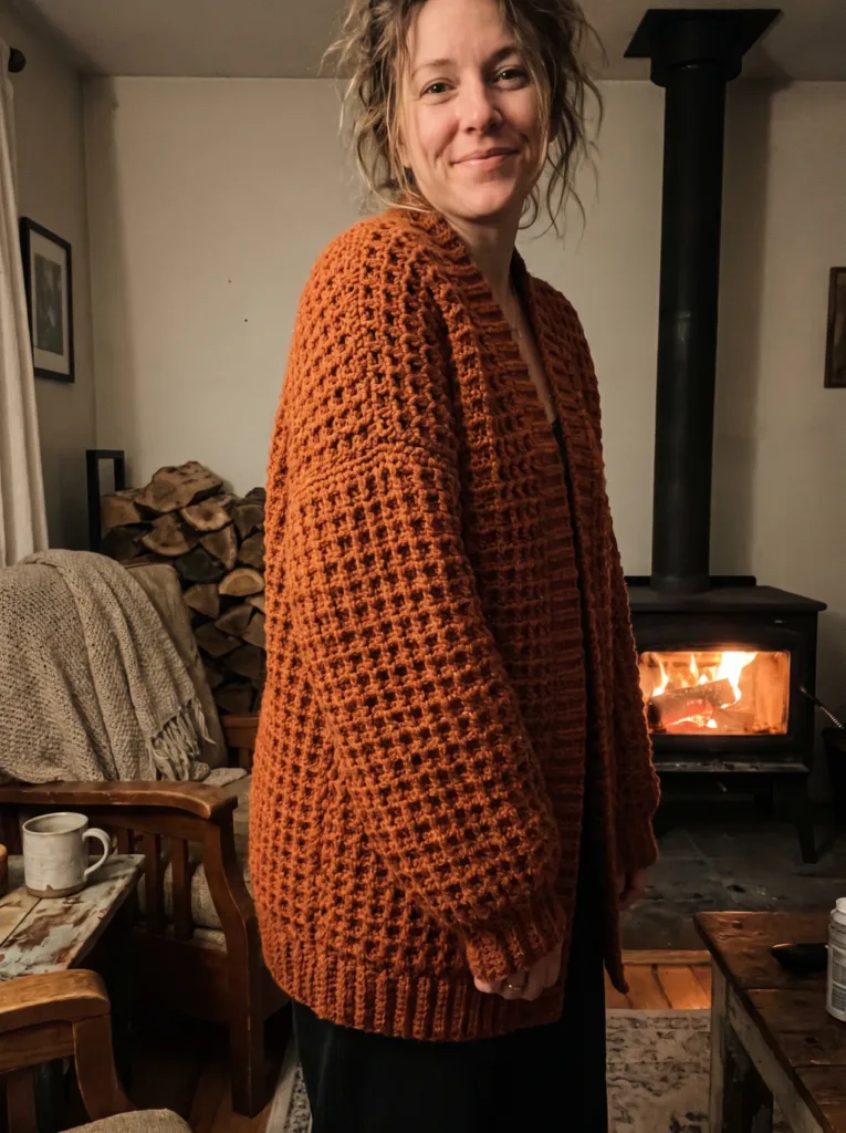 Crochet oversized cardigan in burnt orange waffle stitch with drop shoulders by the fireplace